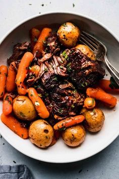 a white bowl filled with meat, potatoes and carrots on top of a table