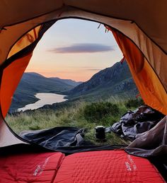 the view from inside a tent looking out at mountains and water in the distance, with sleeping bags on the ground