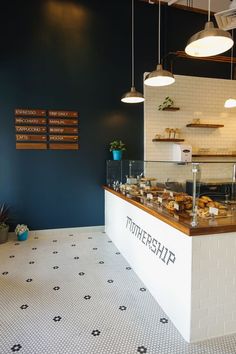 the interior of a bakery with blue walls and white tile flooring, along with hanging lights