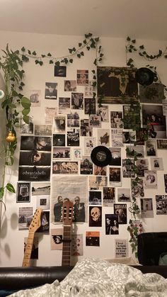 a bedroom wall covered in pictures and plants next to a bed with a guitar on it