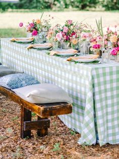 a table set up with flowers and plates on it for an outdoor dinner party in the woods