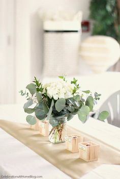 a vase filled with white flowers sitting on top of a wooden table covered in greenery