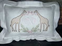 two giraffes on a white pillow with the letter gnf embroidered on it