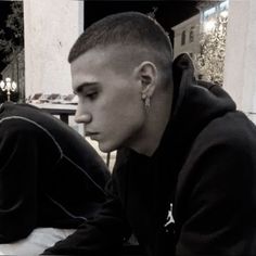 a young man sitting on the ground with his head down and looking at something in front of him