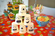 a table topped with lots of cupcakes covered in paper cups and monster faces