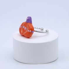 an orange and purple glass pumpkin ring on a white stand with a silver bead