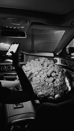 black and white photograph of roses in the back of a car with someone taking a photo