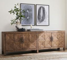 a wooden sideboard with two pictures above it and a plant in the corner next to it