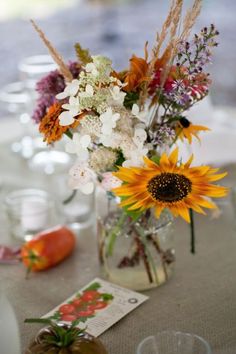 a vase filled with lots of flowers sitting on top of a table next to wine glasses