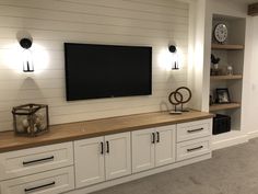 a television mounted on the wall in a living room with white cabinets and black accents