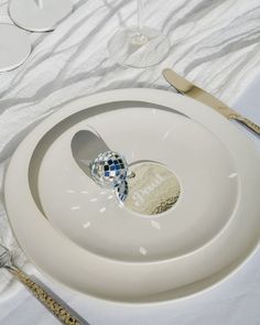 a white plate with spoons and silverware sitting on top of it next to wine glasses