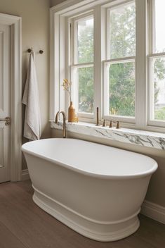 a large white bath tub sitting next to two windows in a bathroom with wooden floors