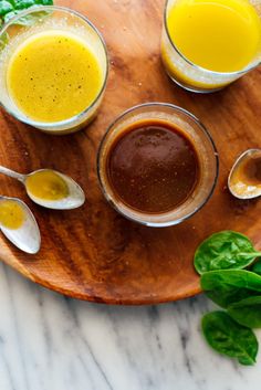 three glasses filled with different colored liquids on top of a wooden plate next to spinach leaves