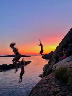 three people jumping off rocks into the water at sunset or dawn with their arms in the air