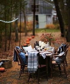 the table is set with wine glasses, plates and napkins on it in the woods