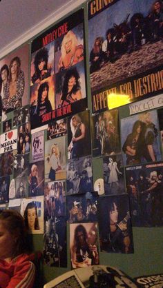 a woman sitting in front of a wall covered with posters