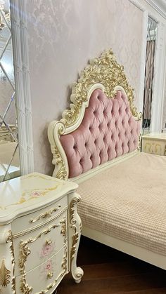 a white bed sitting next to a pink and gold dresser on top of a hard wood floor