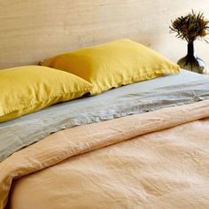 a bed with two yellow pillows on top of it and a vase filled with flowers