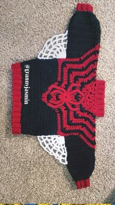 a crocheted black and red mitt laying on the floor