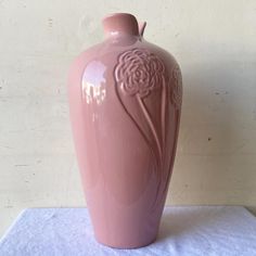 a large pink vase sitting on top of a white tablecloth covered table next to a wall