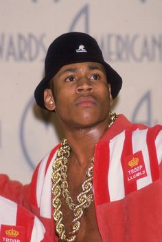 a man wearing a red and white striped jacket with gold chains on his neck, standing in front of a wall