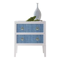 a white vase sitting on top of a blue and white chest of drawers with gold handles