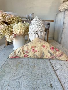 a white vase filled with flowers sitting on top of a table next to a pillow