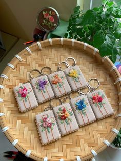 four embroidered key chains sitting on top of a wooden tray next to a potted plant