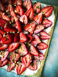 sliced strawberries and pistachios arranged on top of a square pastry crust