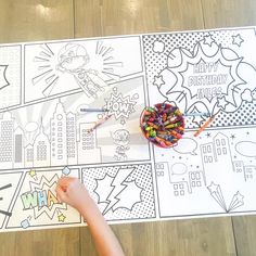 a child's hand pointing at a coloring page on the floor with pencils in it