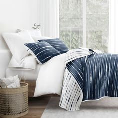 a bed with blue and white comforters in a bedroom next to a basket on the floor