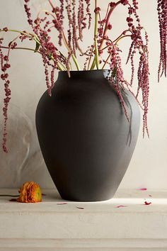 a black vase filled with purple flowers sitting on top of a white shelf next to an orange flower