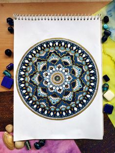 a spiral notebook sitting on top of a table next to rocks and beads, with a drawing of a circular design in the middle