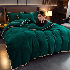 a woman laying on top of a bed covered in a green comforter and pillows