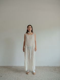 a woman standing in front of a white wall wearing a dress with fringes on it