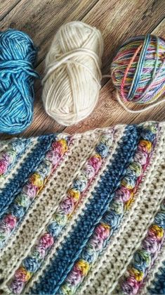 several balls of yarn sitting on top of a wooden floor next to a crocheted blanket