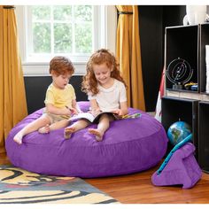 two children are sitting on a bean bag chair and reading the book in their room