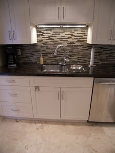 a kitchen with white cabinets and black counter tops, stainless steel dishwasher and sink