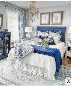 a blue and white bedroom with chandelier, bed, nightstands and pictures on the wall