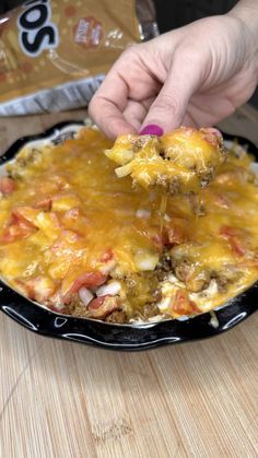 a person is dipping cheese on top of a casserole in a skillet