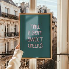 a sign that says take a seat, sweet cheeks on the window sill in front of a building