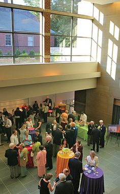 a large group of people standing around tables in a room with high ceilings and floor to ceiling windows