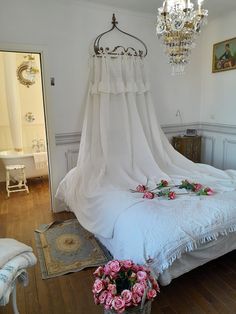 a bed with white sheets and pink flowers on top of it, next to a chandelier