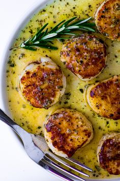 a white plate topped with scallops covered in gravy next to a fork