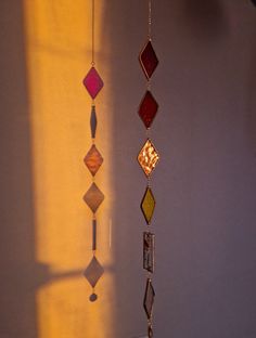 three different colored glass beads hanging from a chain next to a window with the sun shining through it