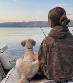 a woman sitting on a boat with her dog and fishing rod in the water behind her