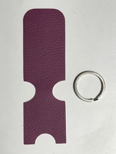 a purple piece of leather next to a silver ring on a white surface with a hole in the middle