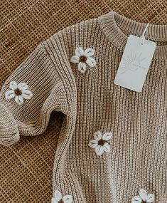 a sweater with white flowers on it sitting on a piece of cloth next to a tag