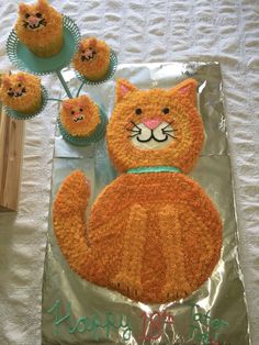 an orange cat cake and cupcakes on a foil wrapper with icing