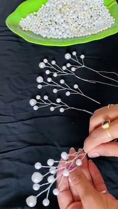 two hands are making beaded flowers on a black tablecloth with a green plate in the background